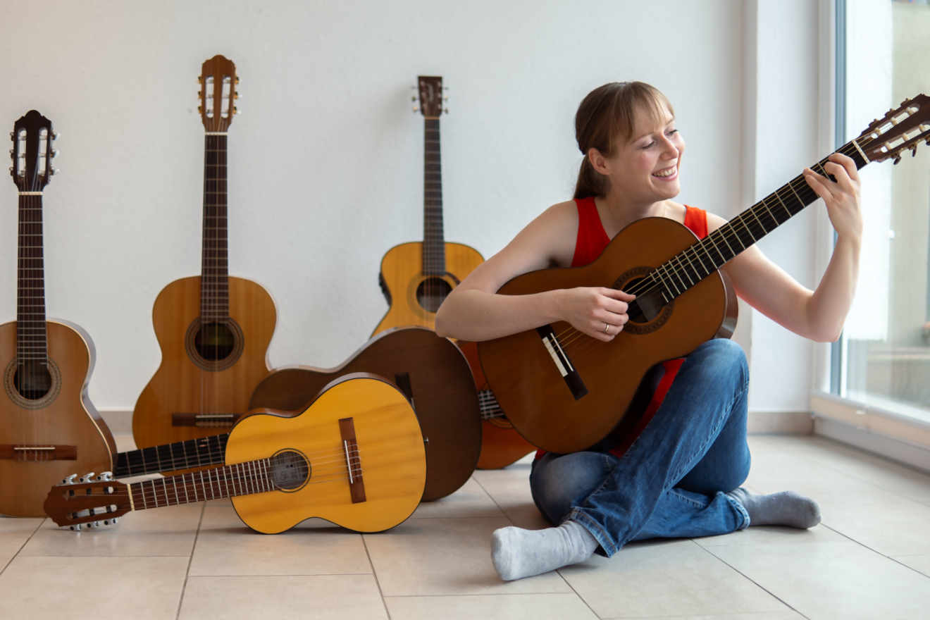 Claudia Kluck sitzt auf dem Boden und spielt Gitarre, neben ihr weitere Gitarren